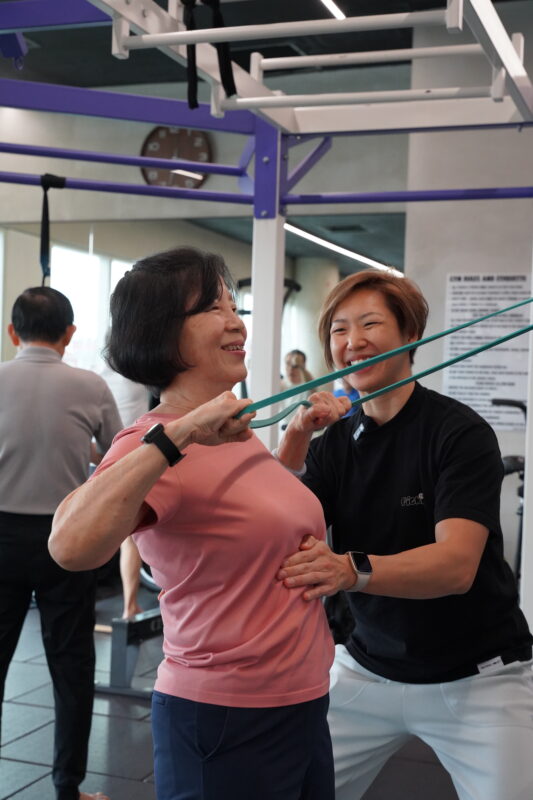A MOVIIN coach guiding a member through a resistance band exercise in the studio